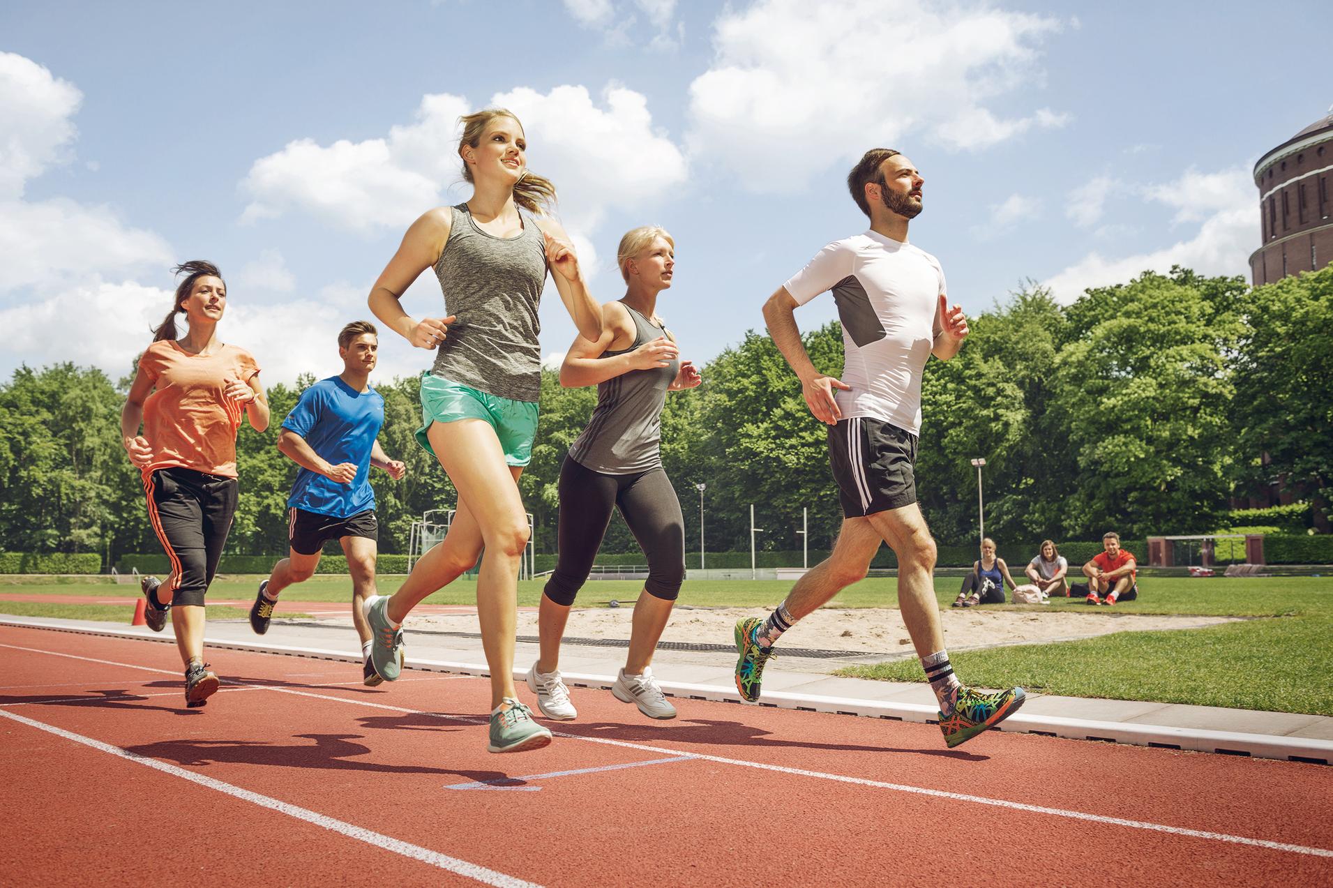 Fünf Erwachsene laufen gemeinsam auf einer Laufbahn im Stadion bei Sonnenschein.